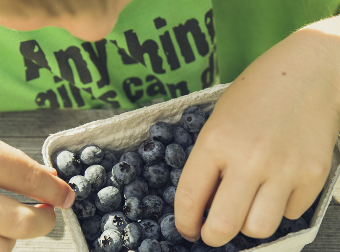A young boy eats a handful of blueberries