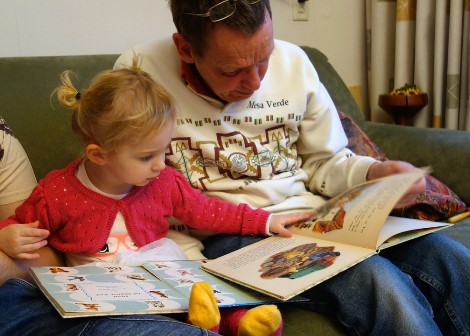 A dad and his daughter read together in a lounge room